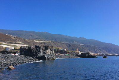 Scenic view of sea and mountains against clear blue sky