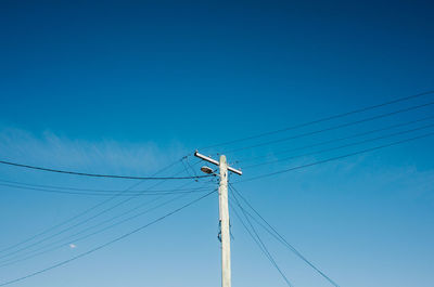 Low angle view of electricity pylon against blue sky