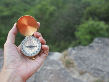 Close-up of hand holding compass against trees