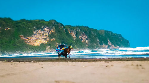 People riding on beach against blue sky