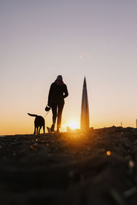 Silhouette of person with dog on beach during sunset