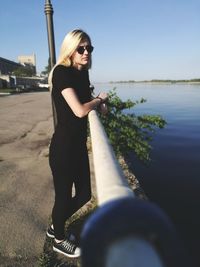 Woman wearing sunglasses standing by water against sky