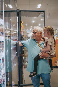 Senior man carrying granddaughter while doing shopping at grocery store