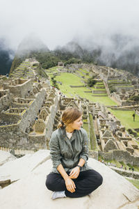 A young woman is sitting near ruins of machu picchu, peru