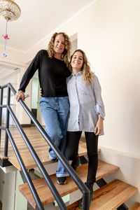 Two female coworkers smiling while posing standing on the stairs at office.