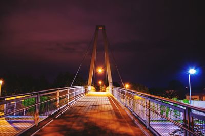 Illuminated footbridge against sky at night