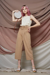 Full length portrait of young woman standing against wall