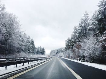 Road amidst trees against sky during winter