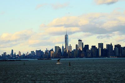 Sea by cityscape against sky during sunset