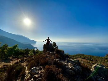 Man sitting on rock by mountain against sky