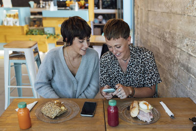 Woman using mobile phone while sitting by friend at restaurant