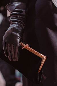 A female hand in a black leather glove holding a classic velvet clutch with a gold frame. 