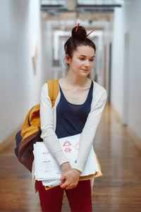 Woman holding papers while standing in corridor