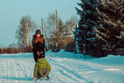 Teenage girl pulling sled on snow covered landscape