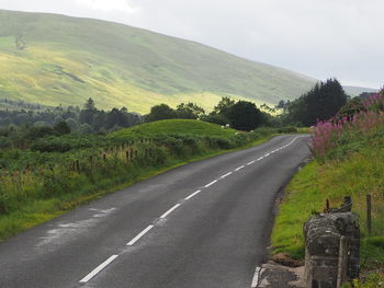 Road amidst trees and landscape against sky