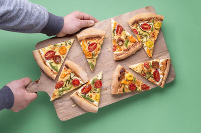 High angle view of hand holding pizza over table against gray background