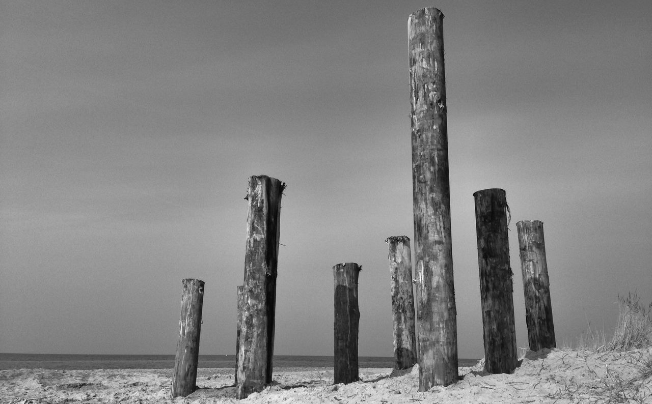 wooden post, wood - material, beach, tranquility, nature, sky, tranquil scene, pole, sand, in a row, sea, day, no people, wooden, outdoors, shore, wood, stack, log, scenics