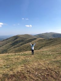 Woman with arms raised standing on hill against sky