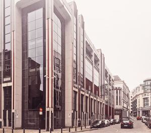 Cars on street by buildings against sky in city