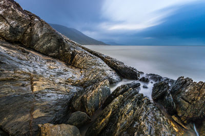 Scenic view of sea by rock formations against cloudy sky