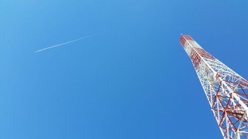Low angle view of vapor trails and communications tower against clear blue sky