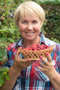 Middle-aged woman picks ripe raspberries in a basket, summer harvest of berries