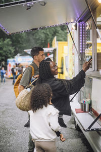 Mother doing contactless payment near food truck while standing with family at amusement park