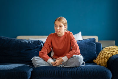 Upset teen girl sitting on sofa at home feeling lonely and frustrated