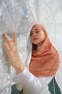 Young woman with arms raised standing against white wall