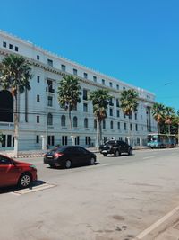 Cars on road by building against blue sky