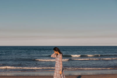 Woman standing at beach against sky