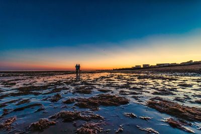 Silhouette person standing on shore by sea against sky during sunset