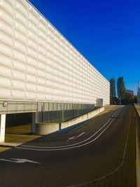 Empty road by buildings against clear blue sky