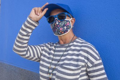 Portrait of senior woman wearing sunglasses and mask standing against blue wall