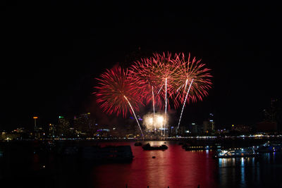 Firework display over illuminated city against sky at night