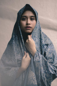 Portrait of young woman with shawl against wall