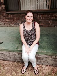 Portrait of smiling young woman standing against brick wall