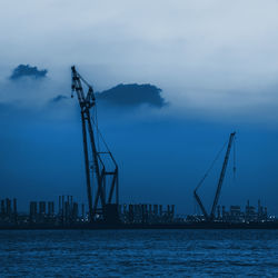 Cranes at harbor against sky