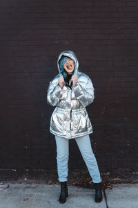 Portrait of young woman standing against brick wall