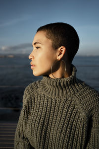 Young woman wearing turtleneck sweater looking away while sitting against sky