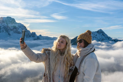 Two female friends taking a selfie in amazing mountains on a sunny day in winter
