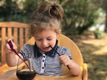 Baby girl with soda holding straw while sitting on chair