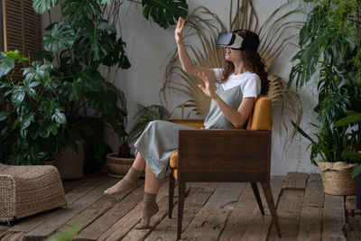 Young amazed woman in vr headset resting at indoor greenhouse full of tropical and exotic plants