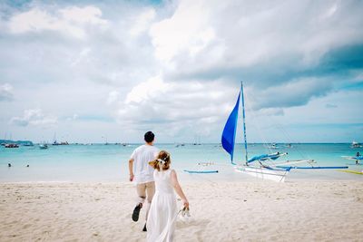 Rear view of men on beach against sky