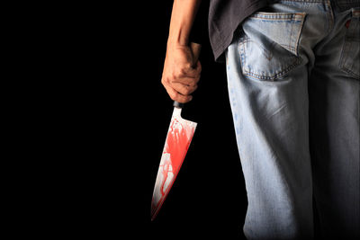 Midsection of man holding knife while standing against black background