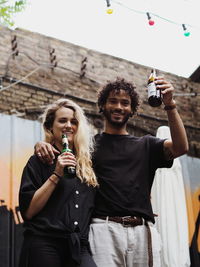 Low angle portrait of smiling friends holding alcoholic drink bottles