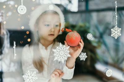 A girl wearing a santa claus hat looks at snowflakes on the window