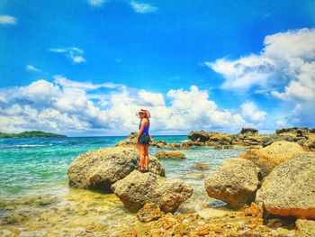 Woman standing on rock by sea against sky