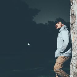 Thoughtful man leaning on tree at night