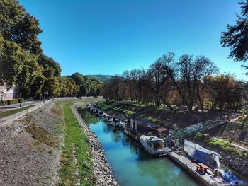 Canal amidst trees against clear blue sky